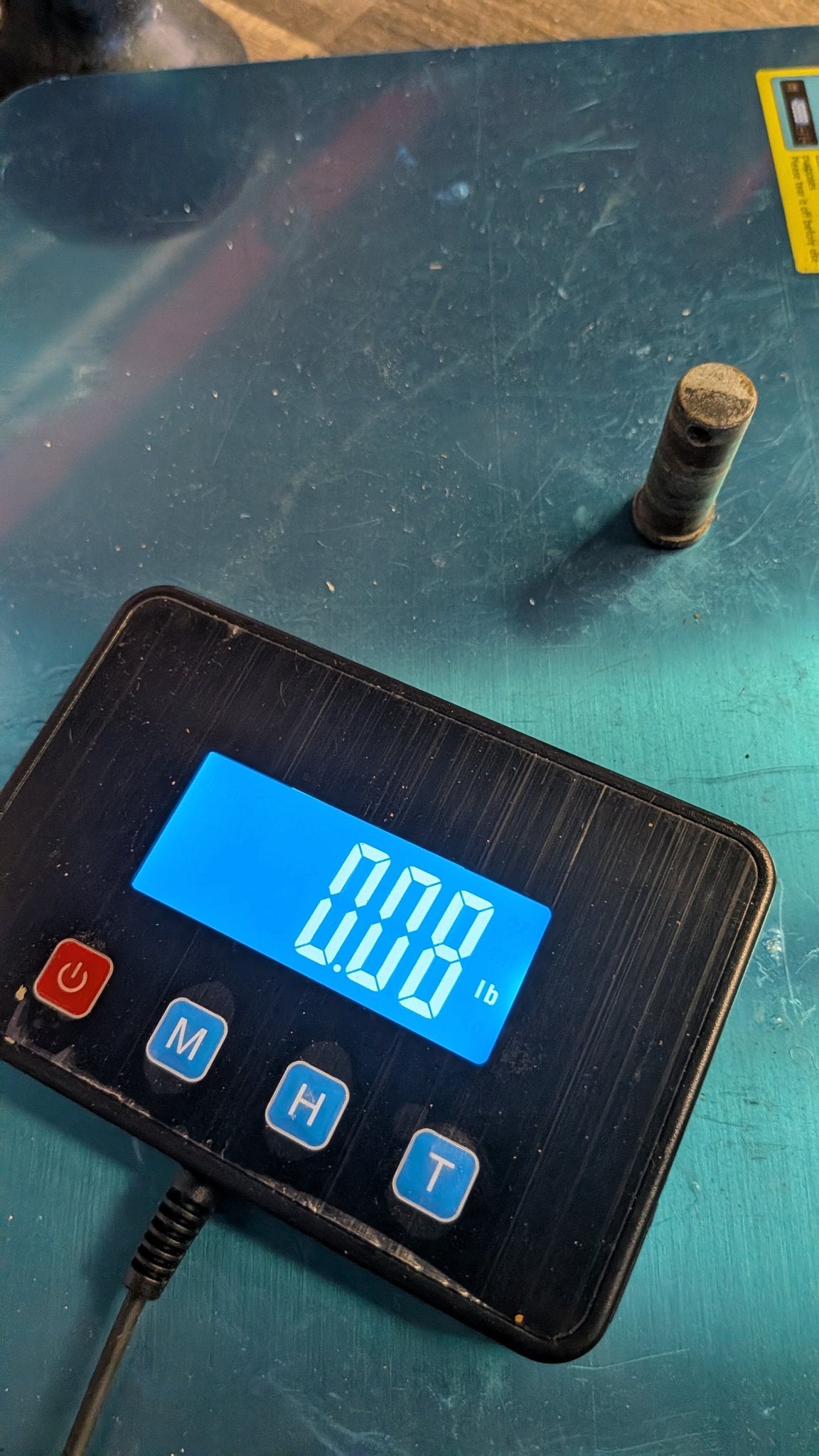 Bronze pivot pin on scale showing 0.00 lb